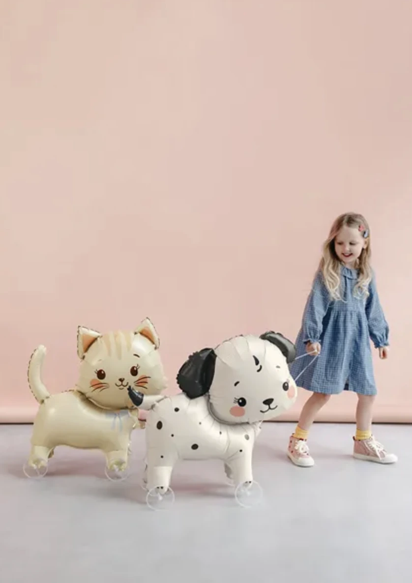 A child walking with wheeled cat and dog foil balloons against a soft pink backdrop.