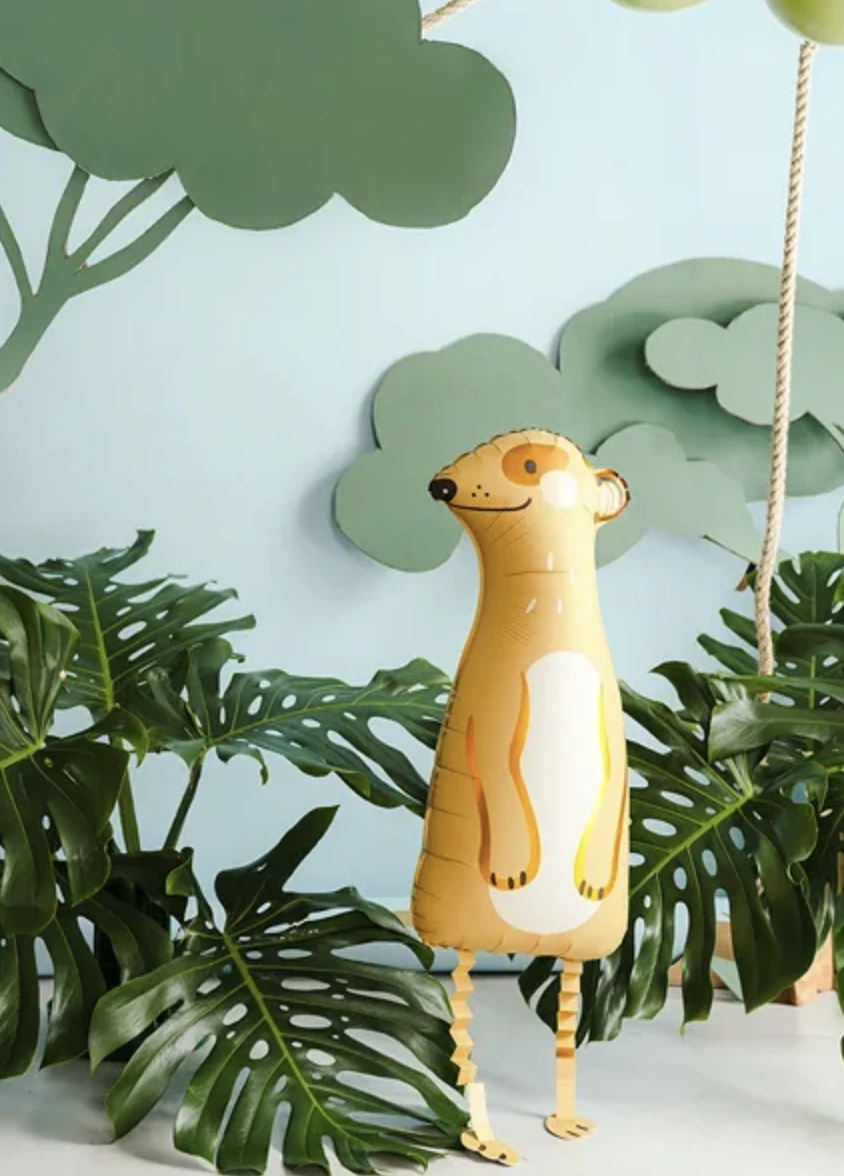 A meerkat foil balloon surrounded by green leaves and paper trees.