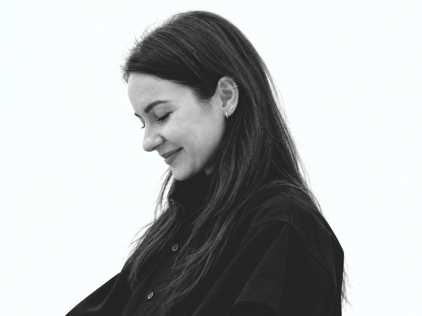 Joanna Hass looking down, in a black shirt. An analog black-and-white portrait.